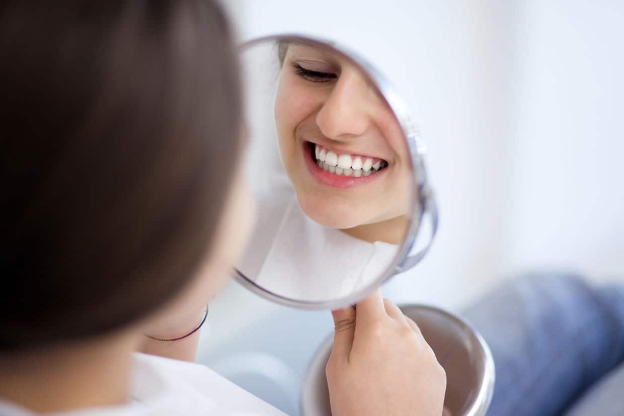 smiling woman looking in a mirror at her one day dental implants